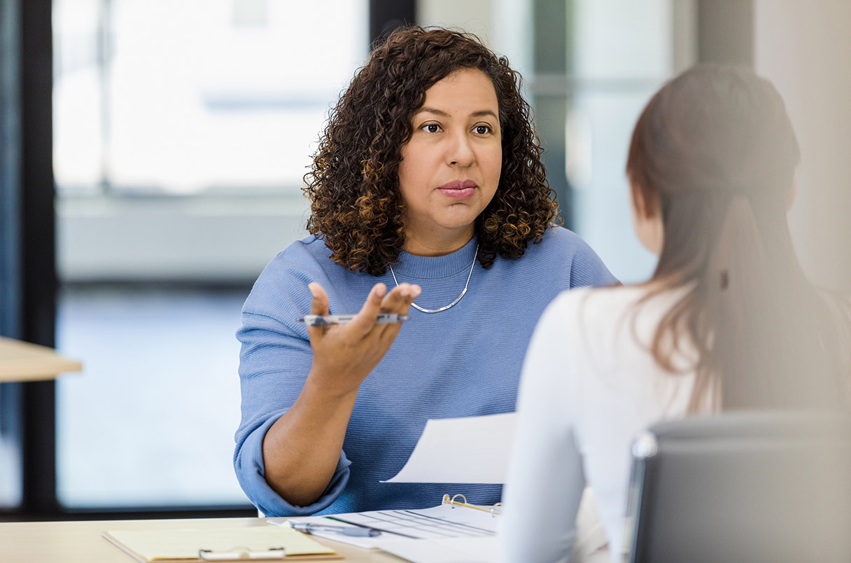 A woman in a supervisory position converses with a younger woman in an office