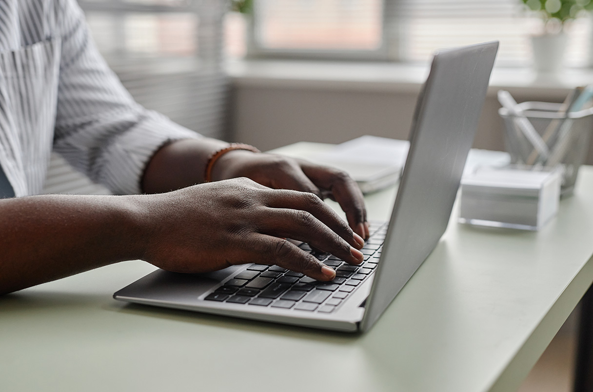 Close up of unrecognizable black man working online , focus on male hands typing at laptop keyboard