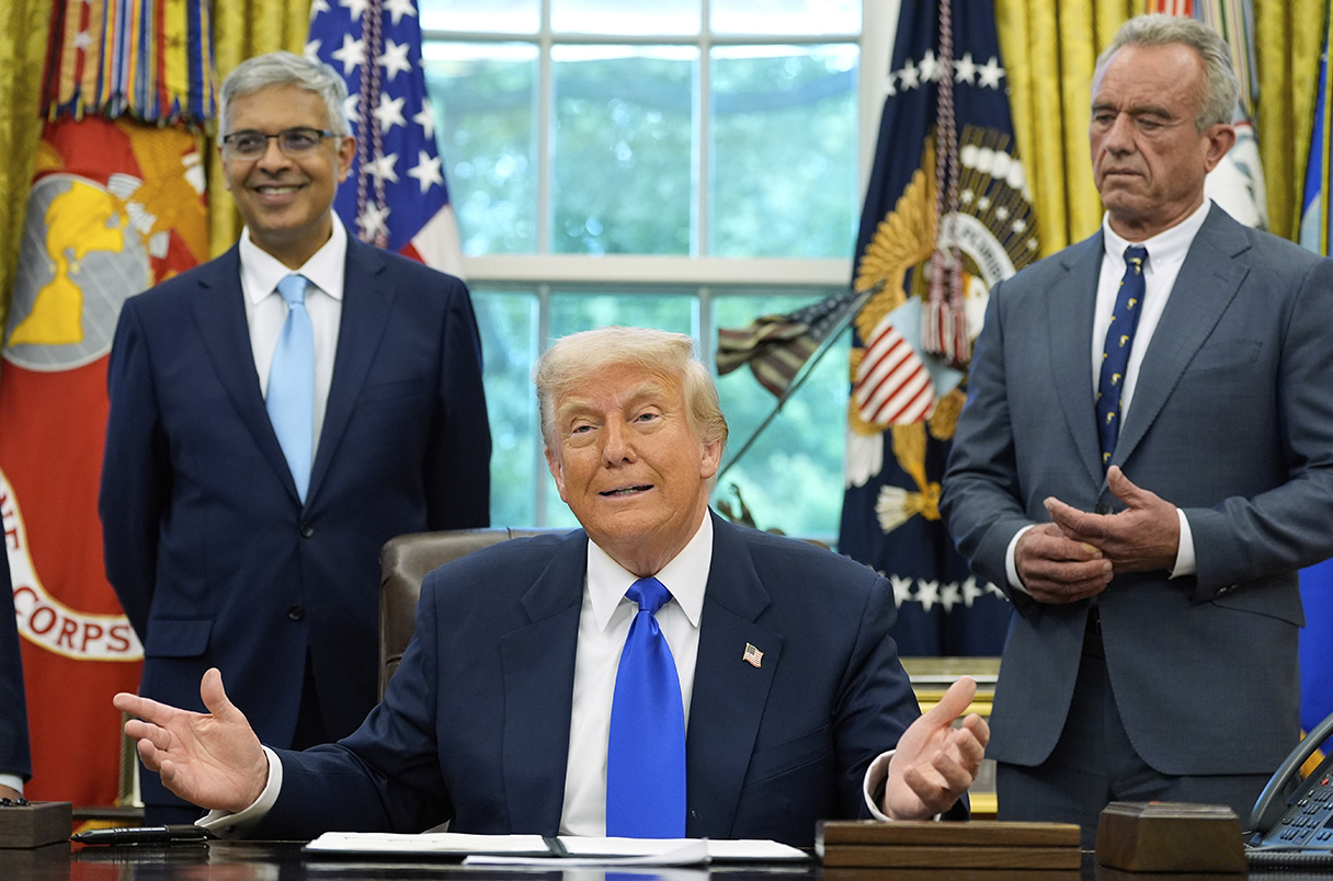 Donald Trump speaks with reporters with Jay Bhattacharya and Robert F. Kennedy Jr. standing behind him
